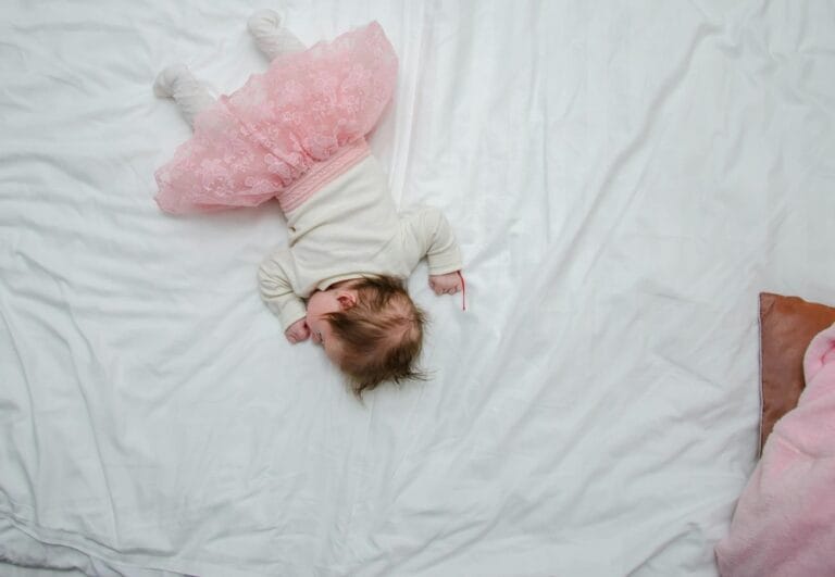 Η εξομολόγηση: Αγνή και τρυφερή εικόνα μωρού σε ροζ φόρεμα, ξαπλωμένο σε λευκό κρεβάτι."