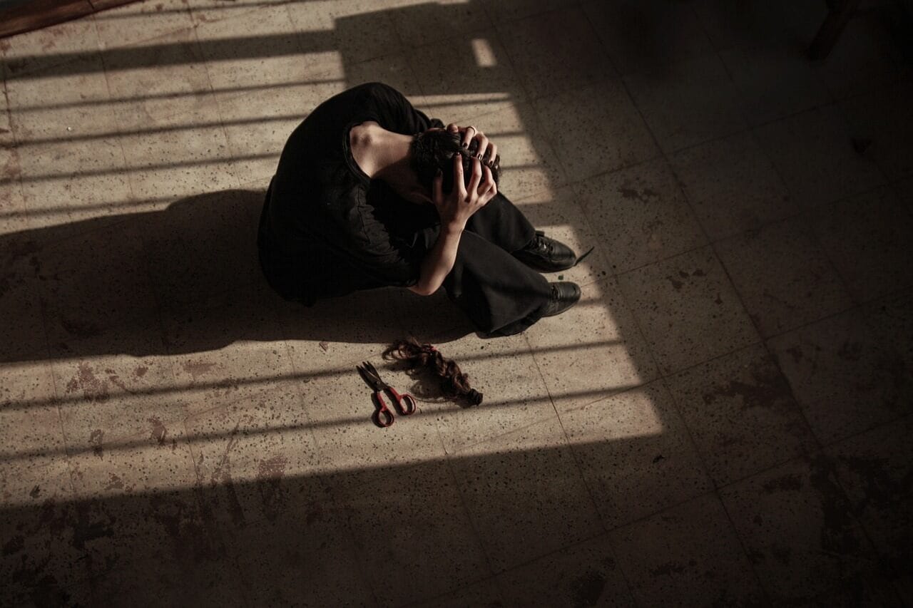 Η Διάφανη καρδιά της γυναίκας καθισμένη στο πάτωμα, μόλις εκοψε τα μαλλιάς της και κρατάει το κεφάλι της. Δίπλα της το ψαλίδι και οι τούφες από τα μαλλιά της,